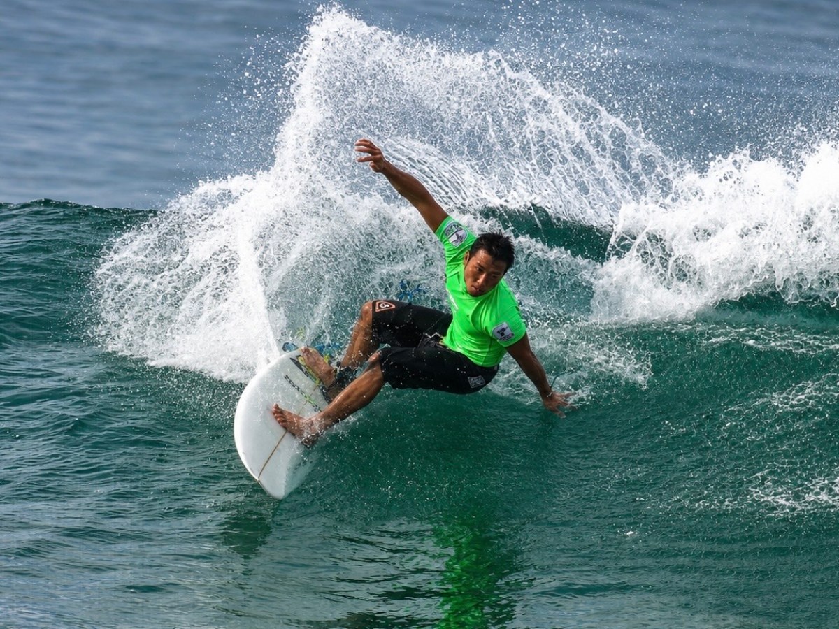 Surfer in green shirt riding a wave with ocean spray.